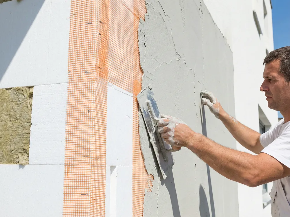 Zatapianie siatki podtynkowej w kleju na elewacji budynku